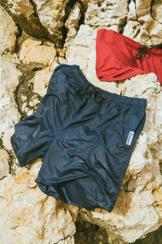 two men swimwear shorts in the colors black and red are drying on a big rock