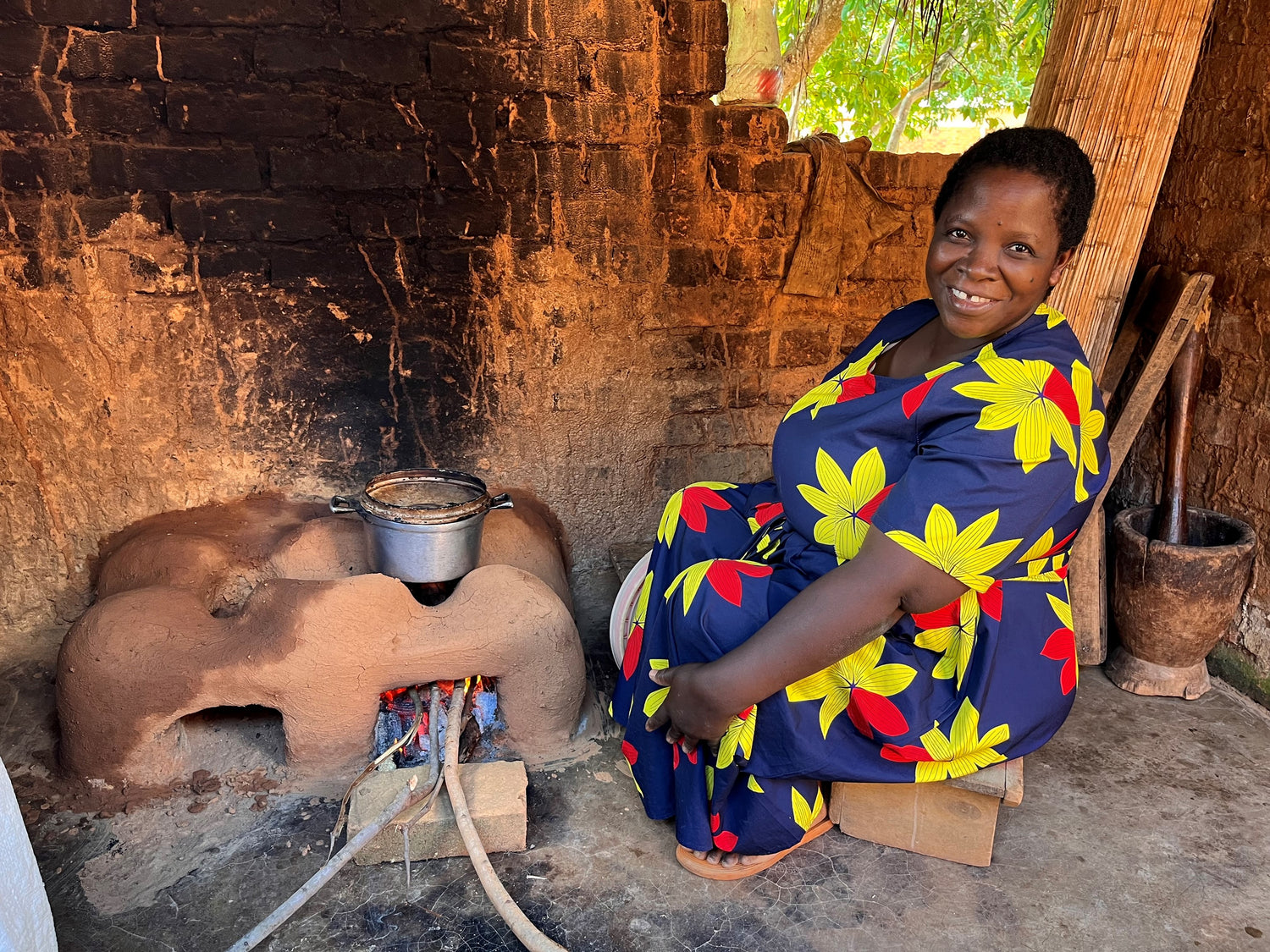 A smiling woman is sitting next to a Changu Changu Moto, this is a cooking stove