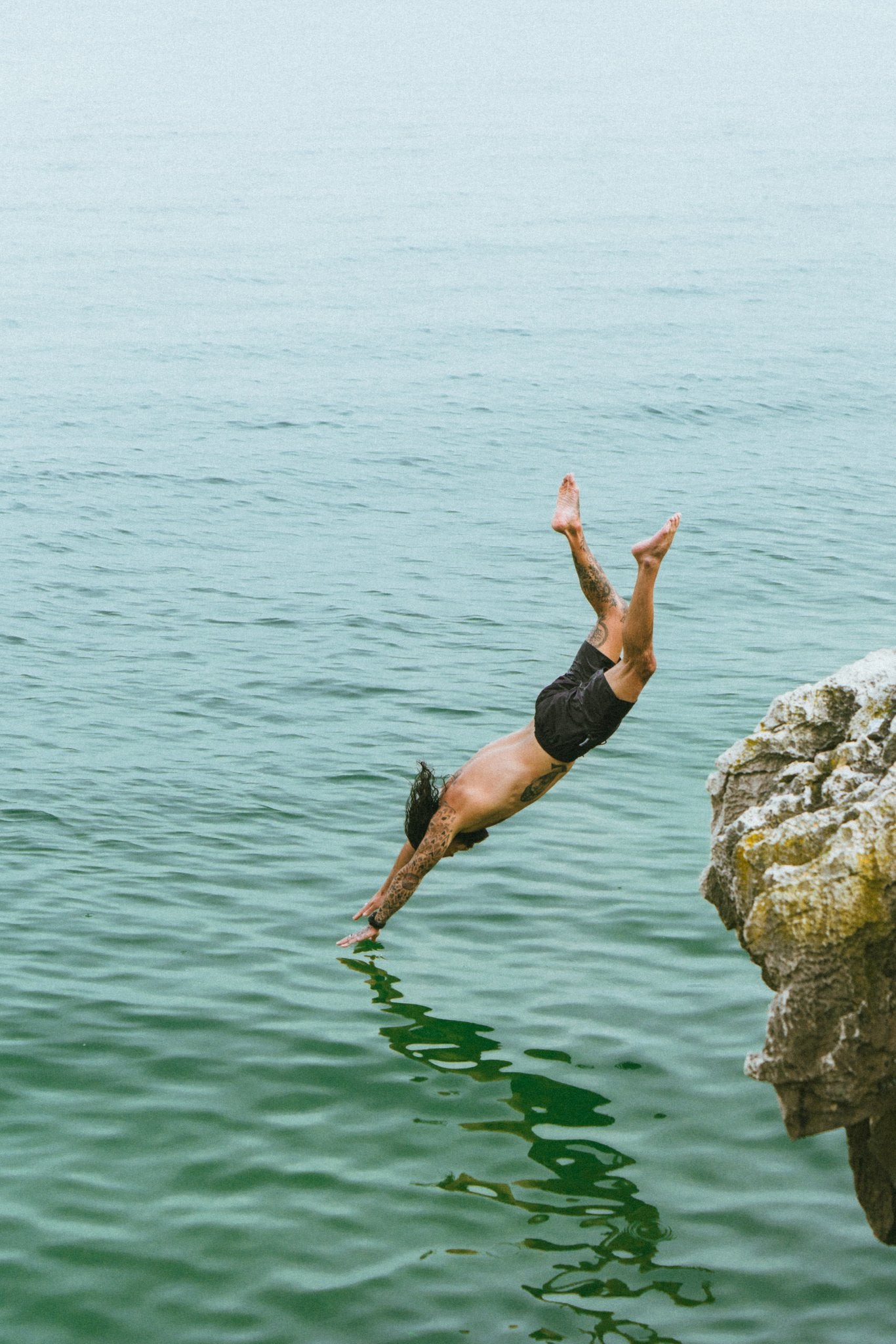 Ein Mann springt von einer Klippe ins Meer. Er trägt eine schwarze Badehose.