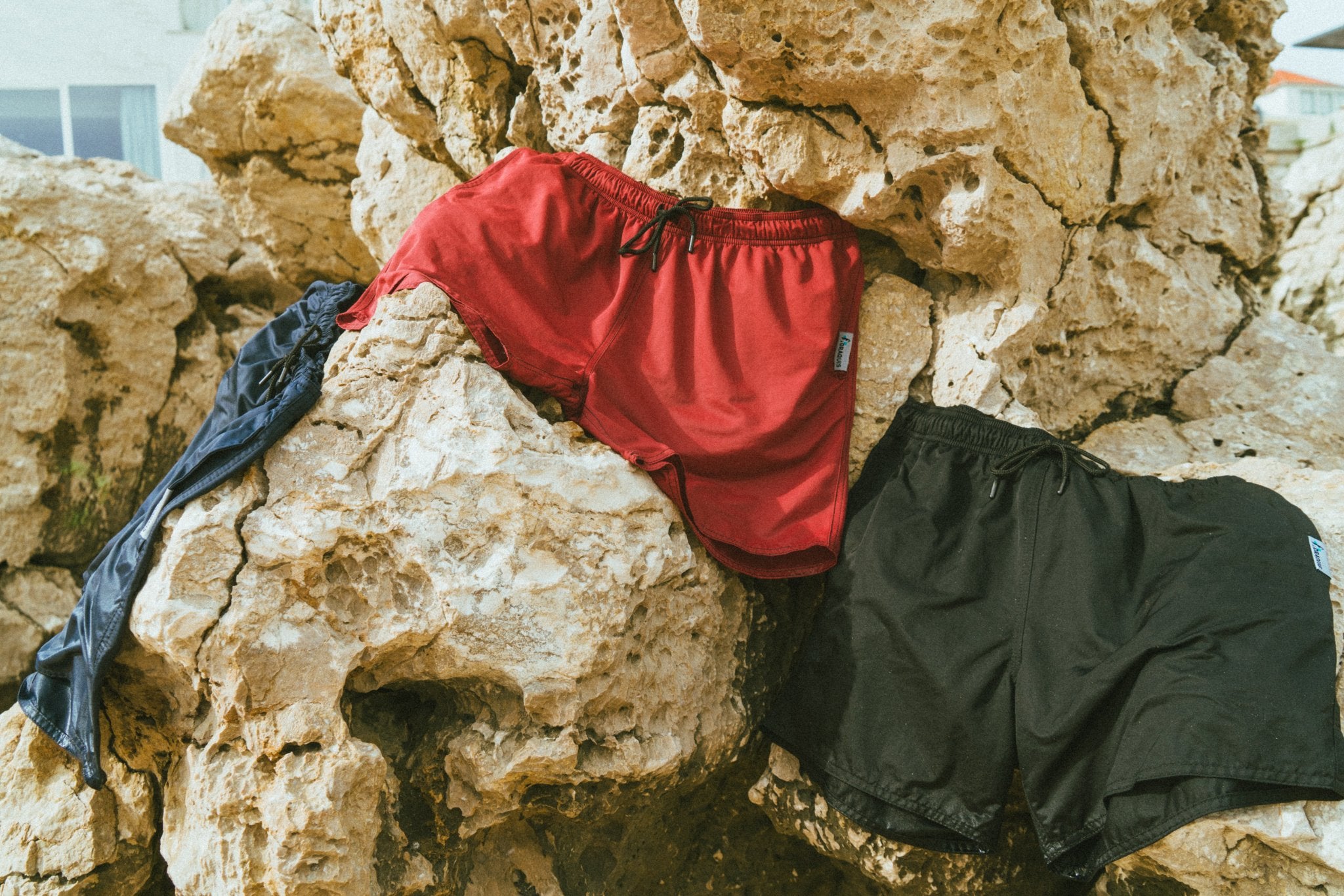 All of the mens swim shorts are drying on rocks. These swim shorts for men are black, blue and red.