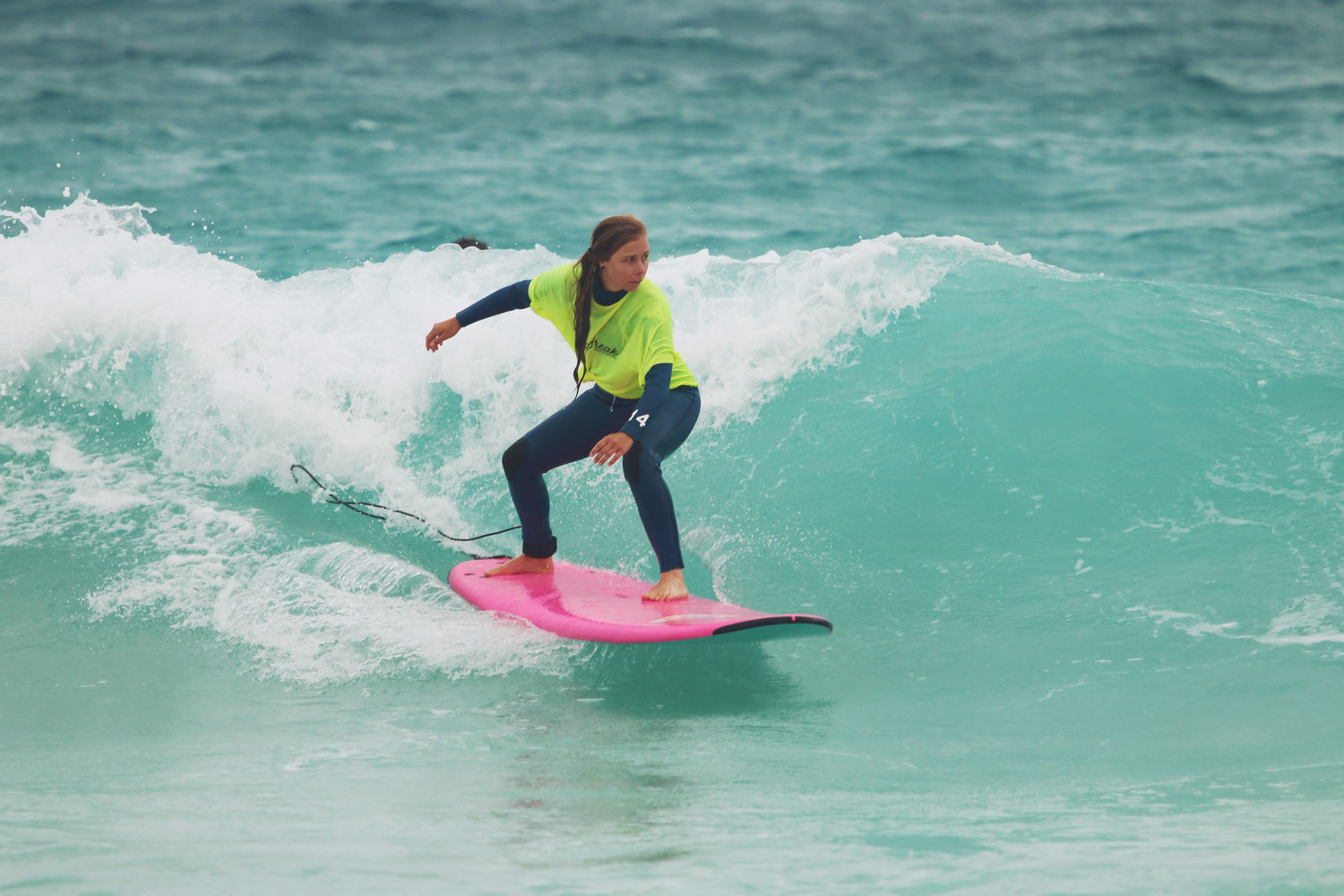 The oprichtster van Draquis is aan het surfen op een groot, fel roze surfboard. ze draagt een wetsuit en een fel geel hesje