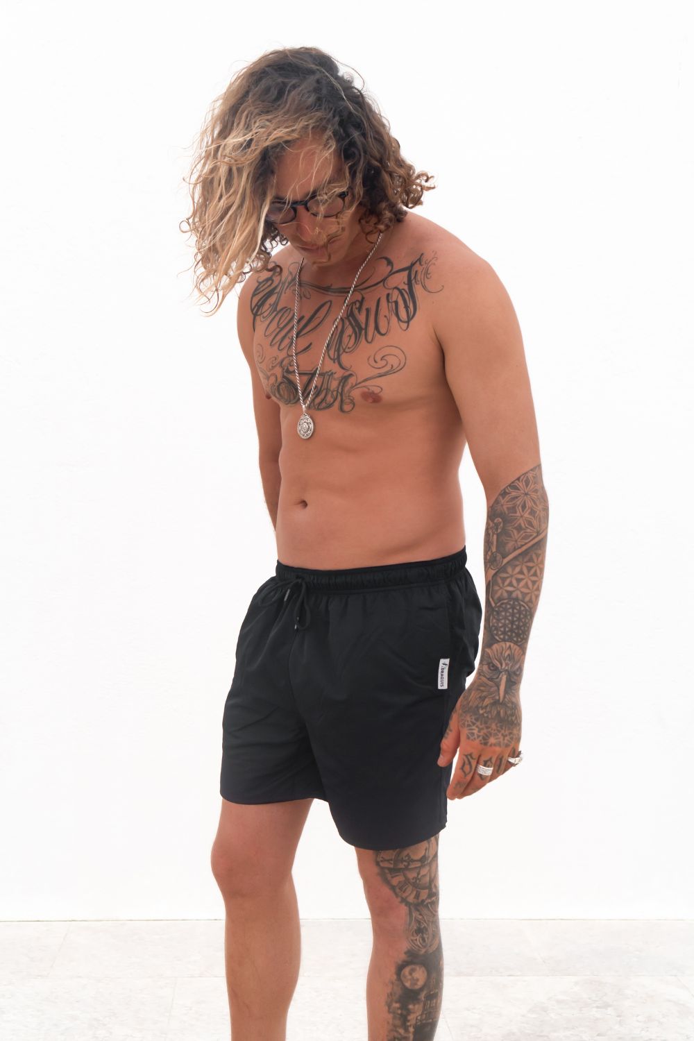 The Cruiser Swim trunks in black from the front, a guy i standing in front of a white wall