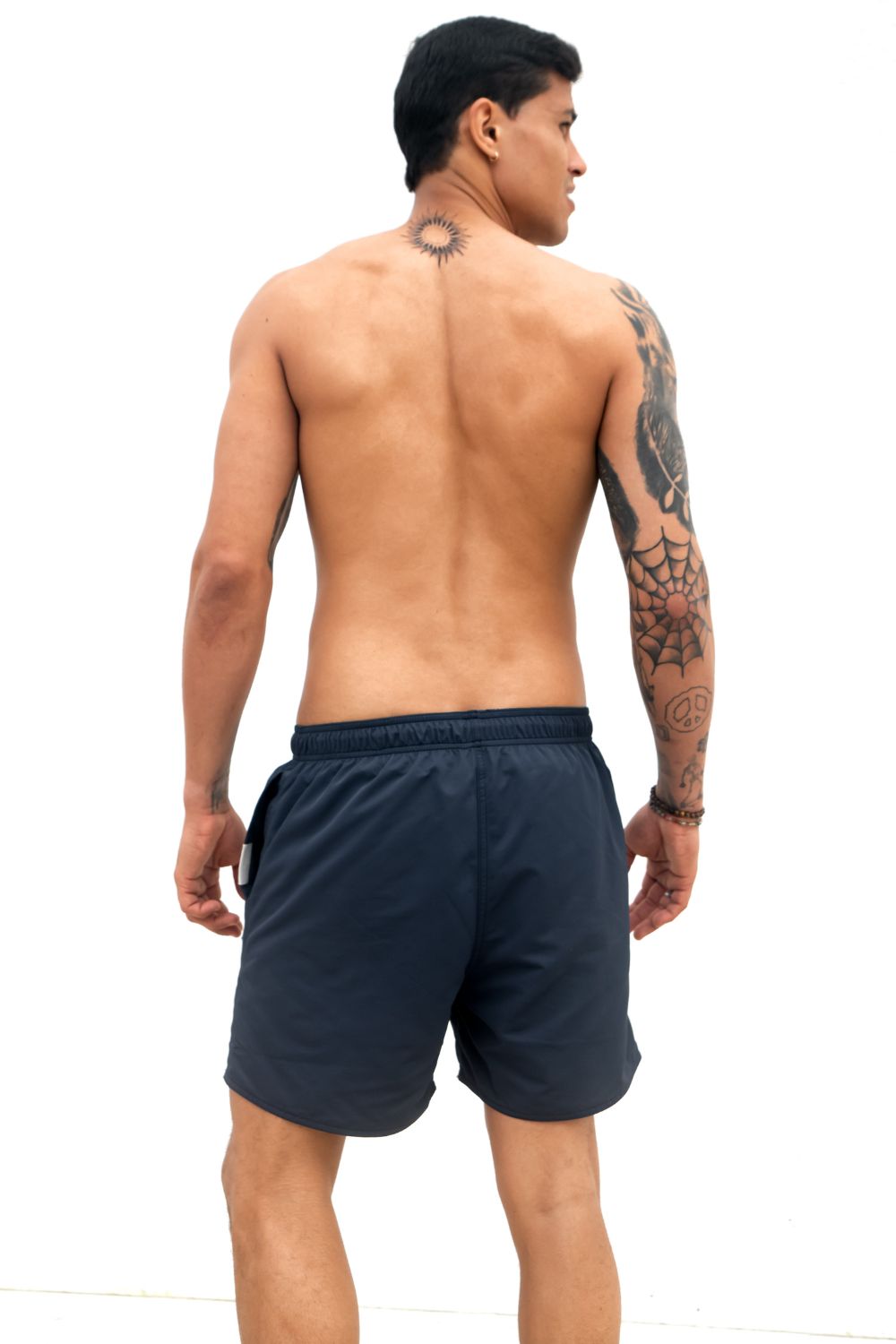 The Cruiser Swim trunks in blue from the back, a guy i standing in front of a white wall