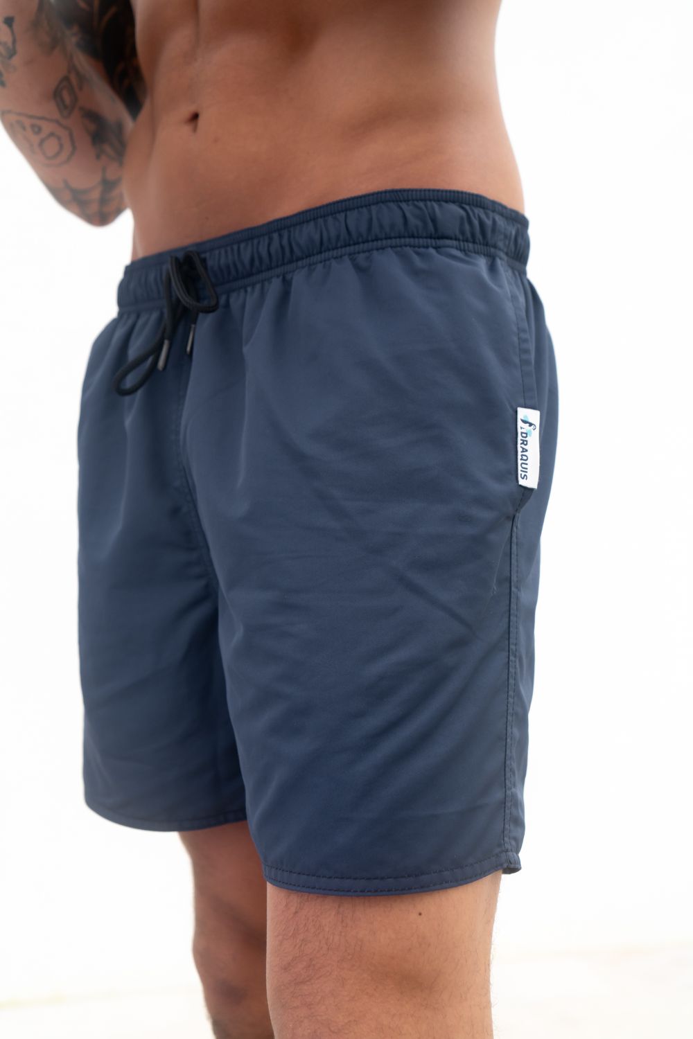 The Cruiser Swim trunks in blue from the front, a guy i standing in front of a white wall