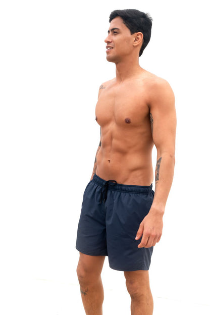 The Cruiser Swim trunks in blue from the front, a guy i standing in front of a white wall