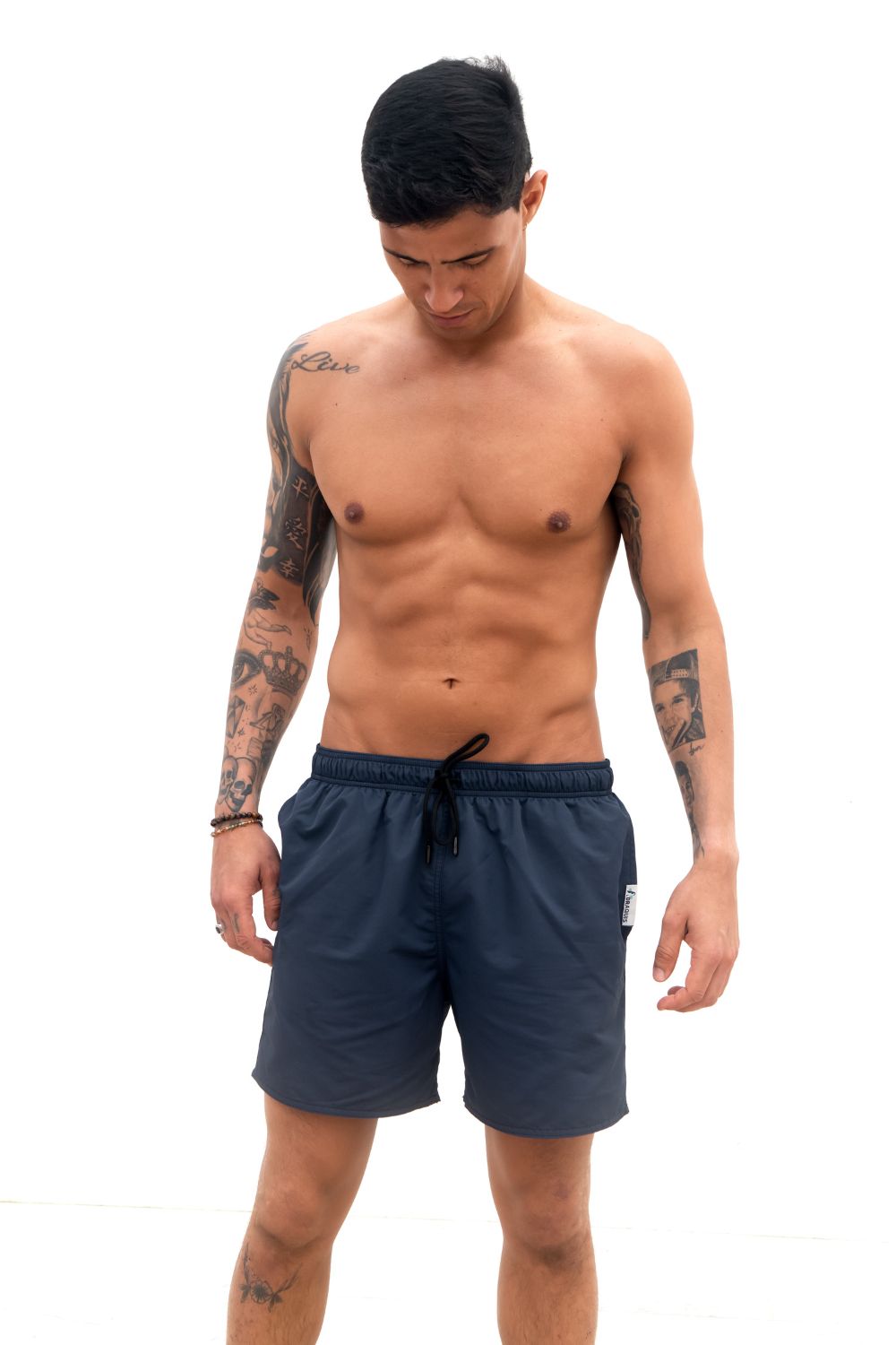 The Cruiser Swim trunks in blue from the front, a guy i standing in front of a white wall