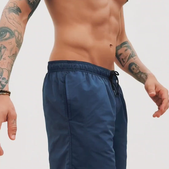  a video of blue swim trunks for men. a guy walking in front of a white wall showing them off