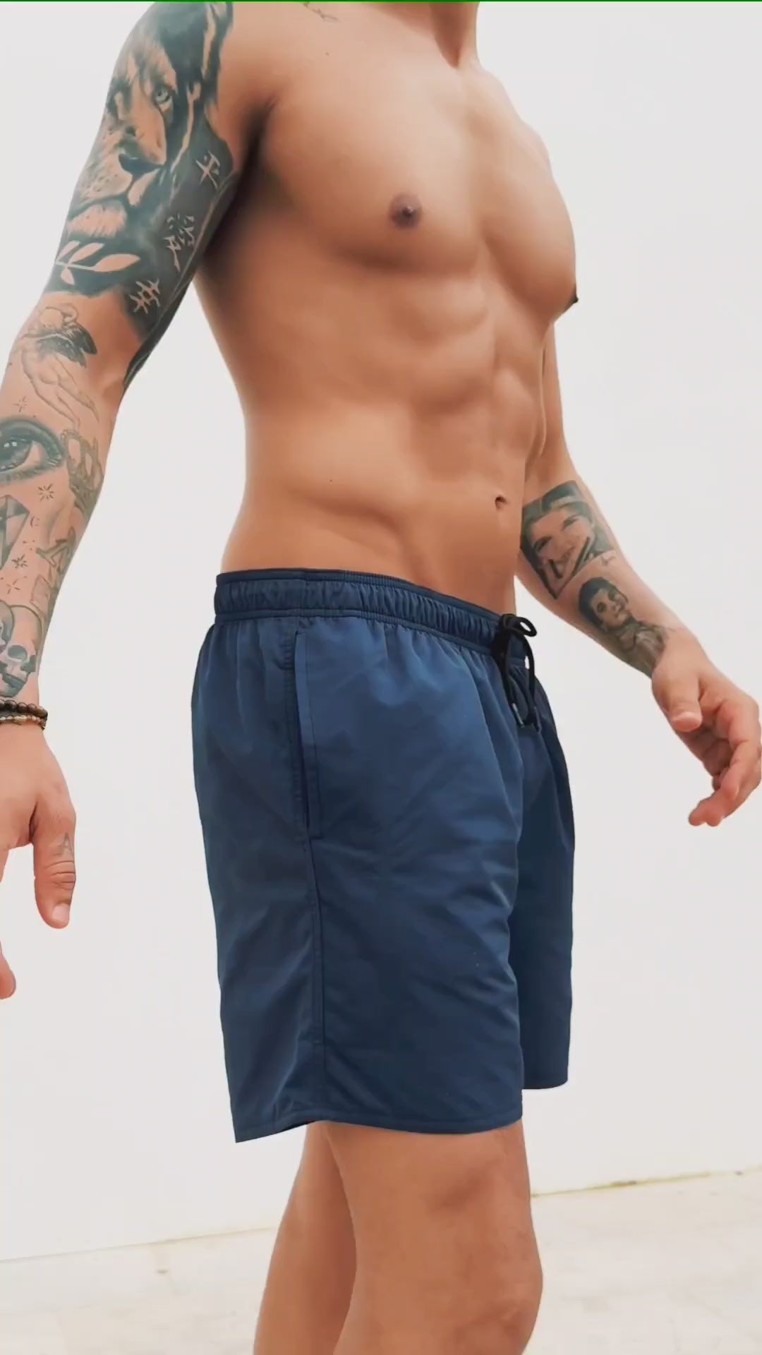  a video of blue swim trunks for men. a guy walking in front of a white wall showing them off