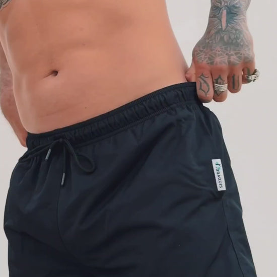  a video of black swim trunks for men. a guy walking in front of a white wall showing them off