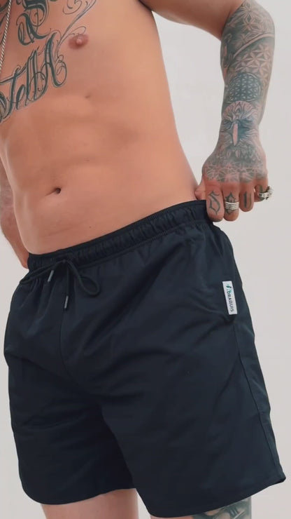  a video of black swim trunks for men. a guy walking in front of a white wall showing them off